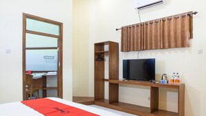 Habitación de hotel con cama, un escritorio de madera con televisor, baño visible a través de una puerta entreabierta y una ventana con cortinas.