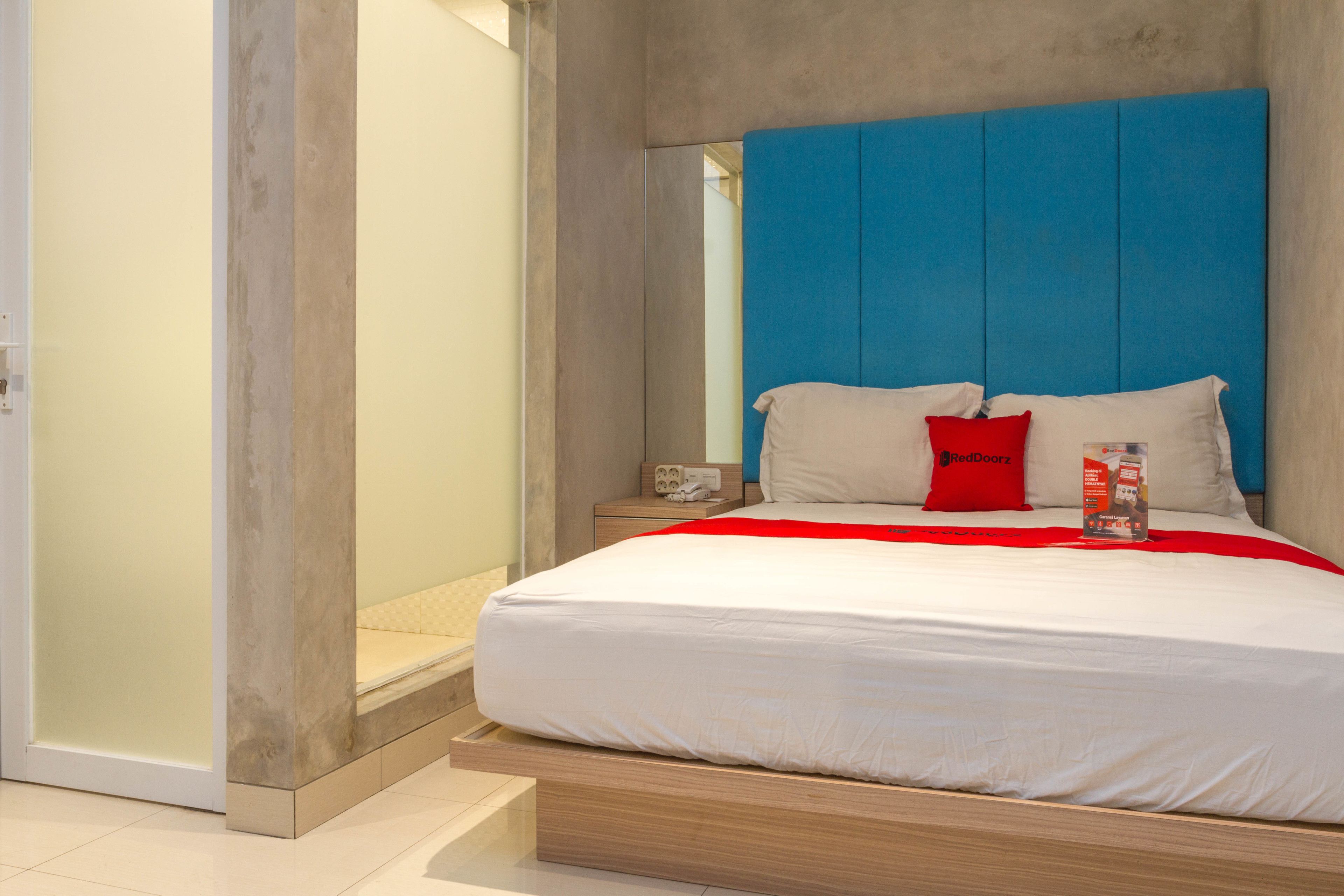 A modern bedroom with a large bed, a blue headboard, and a red pillow.