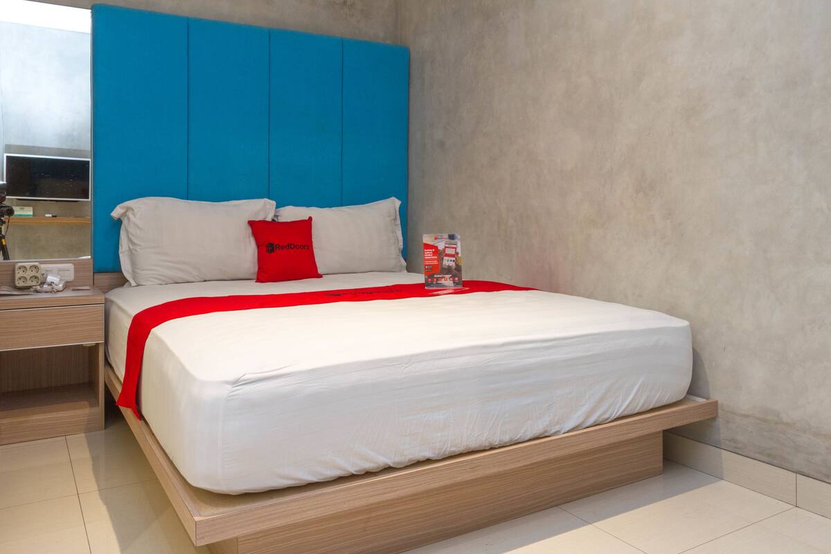Una habitación de hotel moderna con una cama grande, un cabecero azul y una almohada decorativa roja.