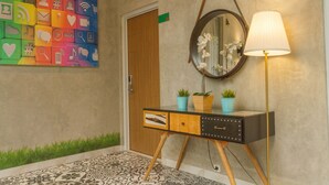 Un couloir moderne agrémenté d’une œuvre d’art murale aux couleurs vives, d’une porte en bois, d’une console sur laquelle sont posées des plantes en pot, d’un miroir et d’un lampadaire.