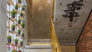 Un escalier avec une rampe jaune, menant à une pièce dont un mur est en briques et dont le plafond est orné d’une fresque.
