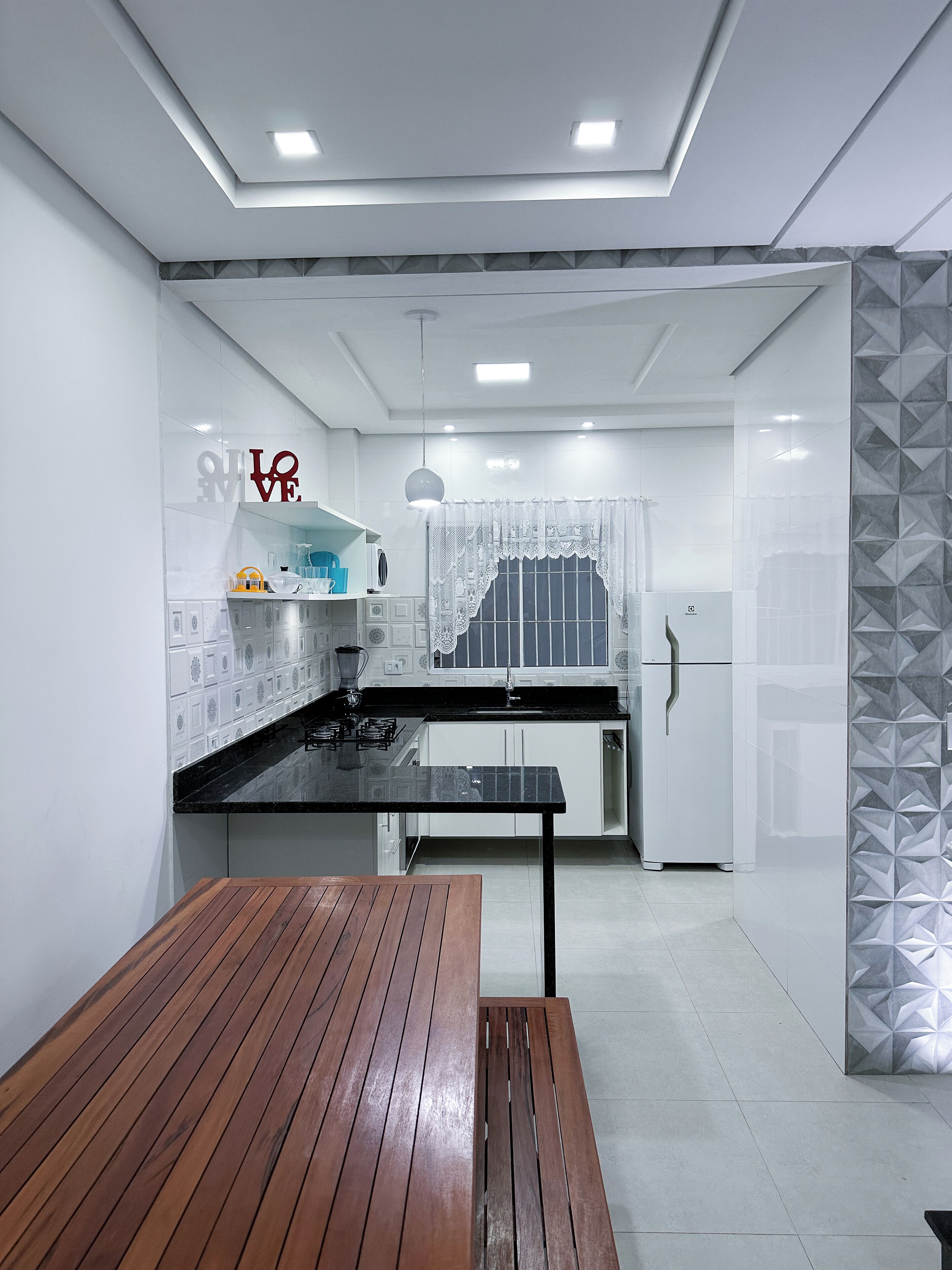 A modern kitchen with white cabinetry, a black countertop, and a wooden dining table.