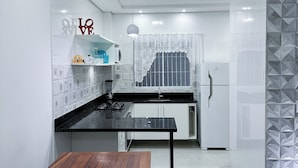 A modern kitchen with white cabinets, a black countertop, and a wooden dining table. - House for vacation in Maranduba/Ubatuba (Maranduba)