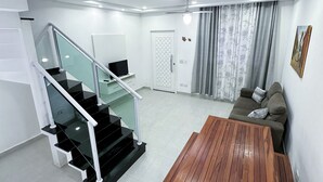 A modern living room with a wooden table, a sofa, a staircase with glass railings, and a door. - House for vacation in Maranduba/Ubatuba (Maranduba)