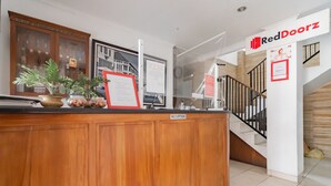 Un mostrador de recepción con detalles de madera, una vitrina de cristal con plantas y un cartel que indica la zona de recepción.