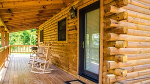 A log cabin with a wooden deck, a rocking chair, and a glass door. - ✧Royale Cabin- KING bed, hot tub, NO CLEANING FEE (Dryfork)