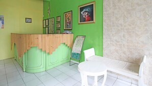 A reception area with a green wall, a wooden reception desk, framed pictures, and a white chair. - RedDoorz near Pojok Beteng Prawirotaman (Yogyakarta)