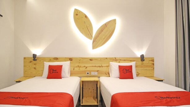A hotel room with two beds, each with a red blanket and a pillow with the hotel logo. The room has a wooden headboard with a unique light fixture above the beds. - RedDoorz near Pojok Beteng Prawirotaman (Yogyakarta)