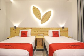 A hotel room with two beds, each with a red blanket and a pillow with the hotel logo. The room has a wooden headboard with a unique light fixture above the beds. - RedDoorz near Pojok Beteng Prawirotaman (Yogyakarta)