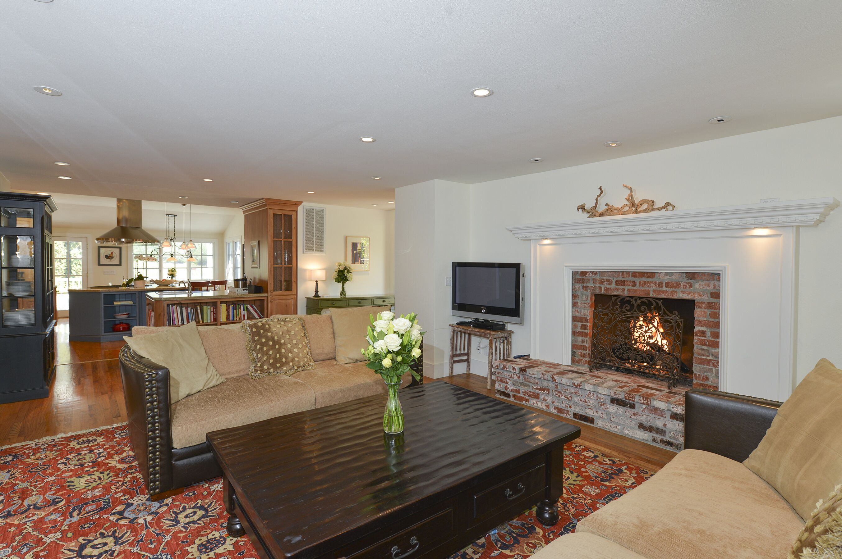 A living room with a fireplace, a television, and a coffee table with a vase of flowers.