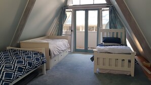 A dorm-style room with two single beds, a sliding glass door to the balcony, and a sloped ceiling.