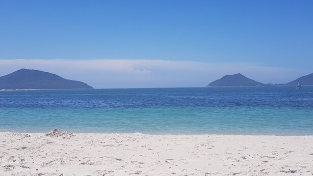A beach with clear turquoise water, white sand, and two small islands in the distance.