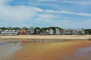 A beachfront property with a sandy beach, a row of houses, and a clear sky. - Beachfront on Commercial St w/ Water Views! (Provincetown)