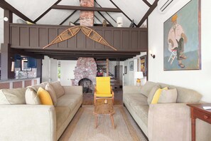 Ein Wohnzimmer mit zwei Sofas, einem Couchtisch aus Holz, einem gelben Sessel, einem Kamin und einem Bild an der Wand.