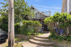 A residential area with a staircase leading to a balcony, surrounded by greenery and a parked car.