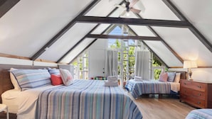 Ein schräges Schlafzimmer im Dachgeschoss mit zwei Betten, Holzboden und Deckenventilator.