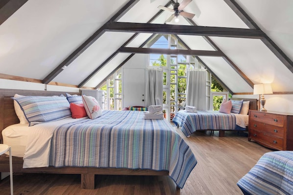 Une chambre mansardée de forme triangulaire, avec deux lits, un plancher en bois et un ventilateur de plafond.