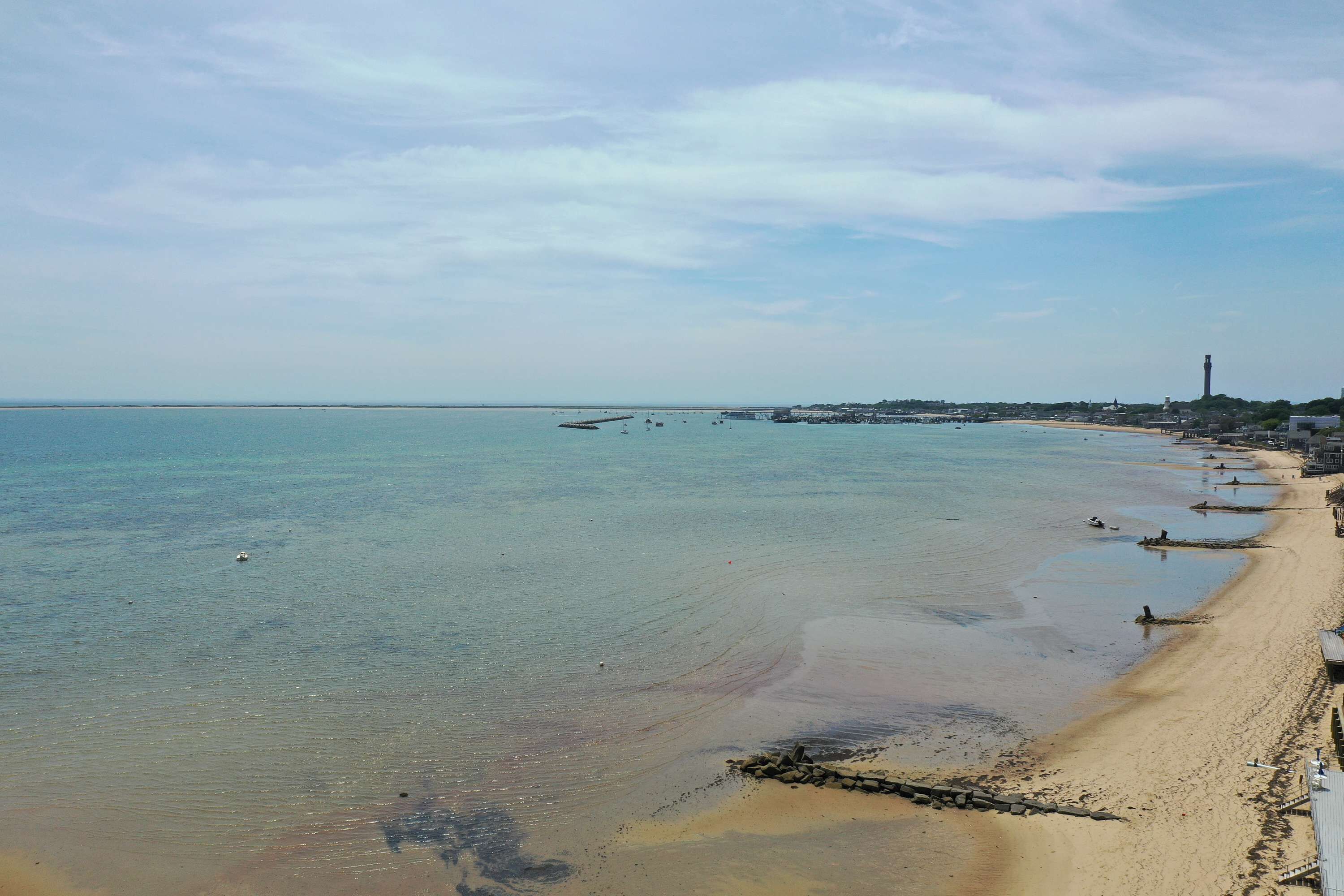 Una playa con agua cristalina, una orilla arenosa y un faro a lo lejos.