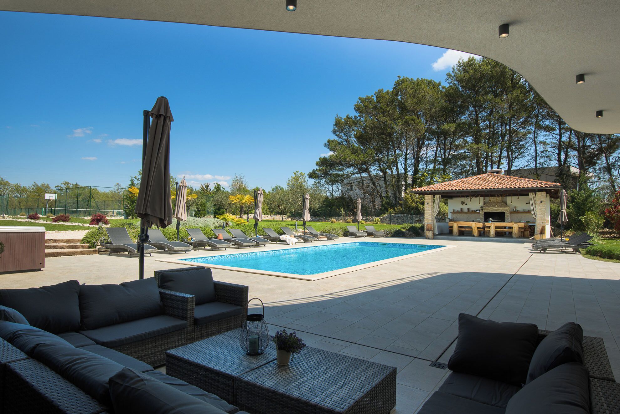 Un espace piscine doté de chaises longues, d’un coin salon abrité et offrant une vue sur le paysage environnant.
