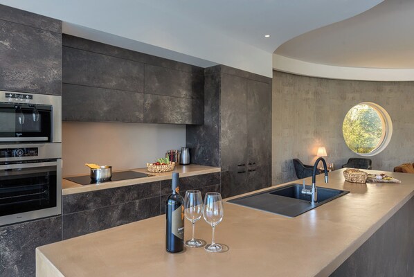 A modern kitchen with a central island, built-in ovens, and a large window providing a view of greenery.