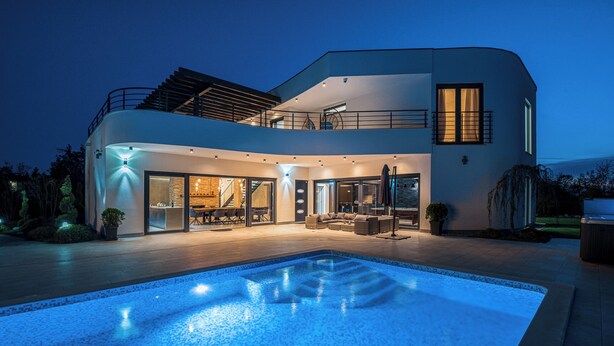 Une maison moderne à deux étages, dotée d’une piscine, de grandes fenêtres et d’un balcon.