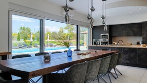 Une cuisine moderne dotée d’un grand îlot central, d’un coin repas avec des chaises et d’une vue sur une piscine.