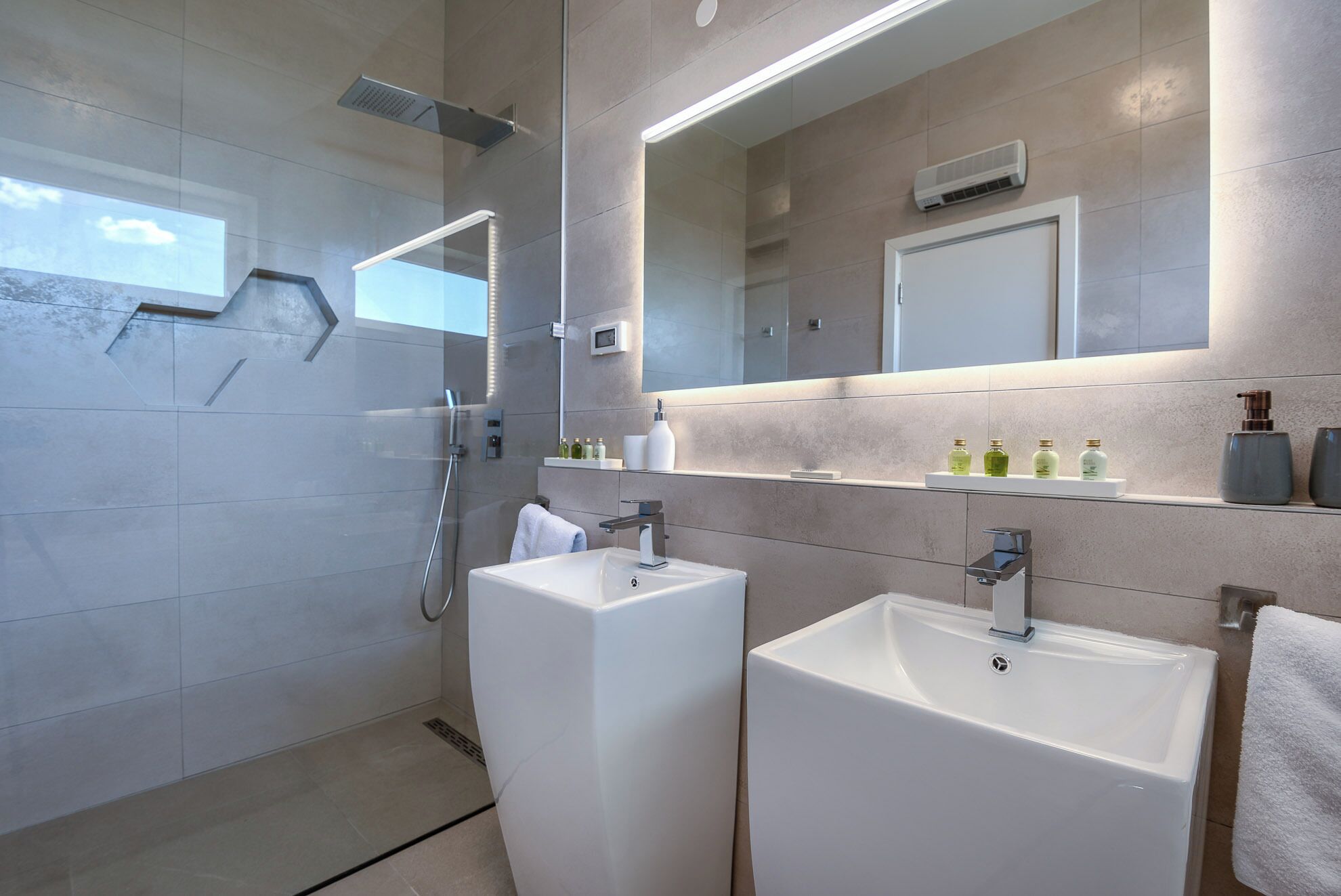 Une salle de bain moderne avec deux lavabos, une douche et un grand miroir.