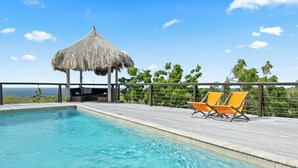 A swimming pool with two orange lounge chairs and a thatched-roof structure. - Amazing 360 views over the Caribbean Sea, 12 guests and private pool (Sint Willibrordus)