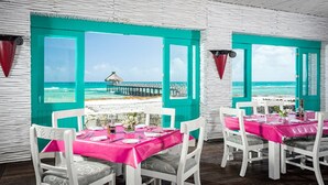 A dining area with turquoise walls and white furniture, overlooking a beach and pier.