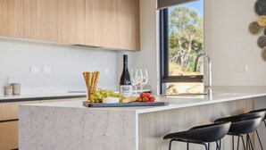 A modern kitchen with a marble countertop, a wine bottle, glasses, and a variety of snacks. - Chilam B embraces open plan living with a combined kitchen/ dining/ living area (Jindabyne)