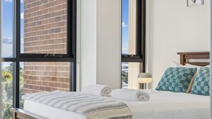 A hotel room with a large window, a bed with white linens, two rolled towels, and a headboard with patterned pillows. - Chilam B embraces open plan living with a combined kitchen/ dining/ living area (Jindabyne)