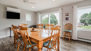 A dining room with a wooden table and chairs, a ceiling fan, and large windows with curtains. - Beautiful Cottage Overlooking Bear Lake (Bear Lake)