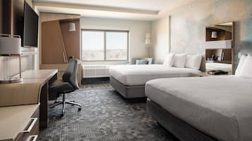 Une chambre d’hôtel avec un bureau, deux lits, une télévision et une grande fenêtre.