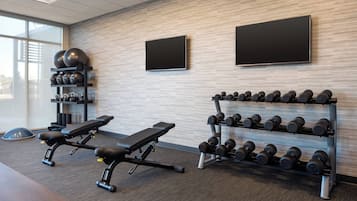 Une salle de sport équipée de matériel d’exercice, notamment des bancs, des haltères et des ballons d’exercice.