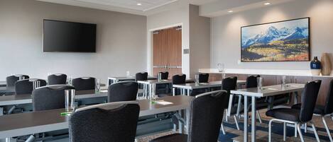 A conference room with tables and chairs, a flat-screen TV, and a large landscape painting on the wall.