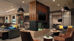 A modern lounge area with sofas, armchairs, a fireplace, and a bar area with a television and bar equipment. - Courtyard by Marriott Loveland Fort Collins (Loveland)
