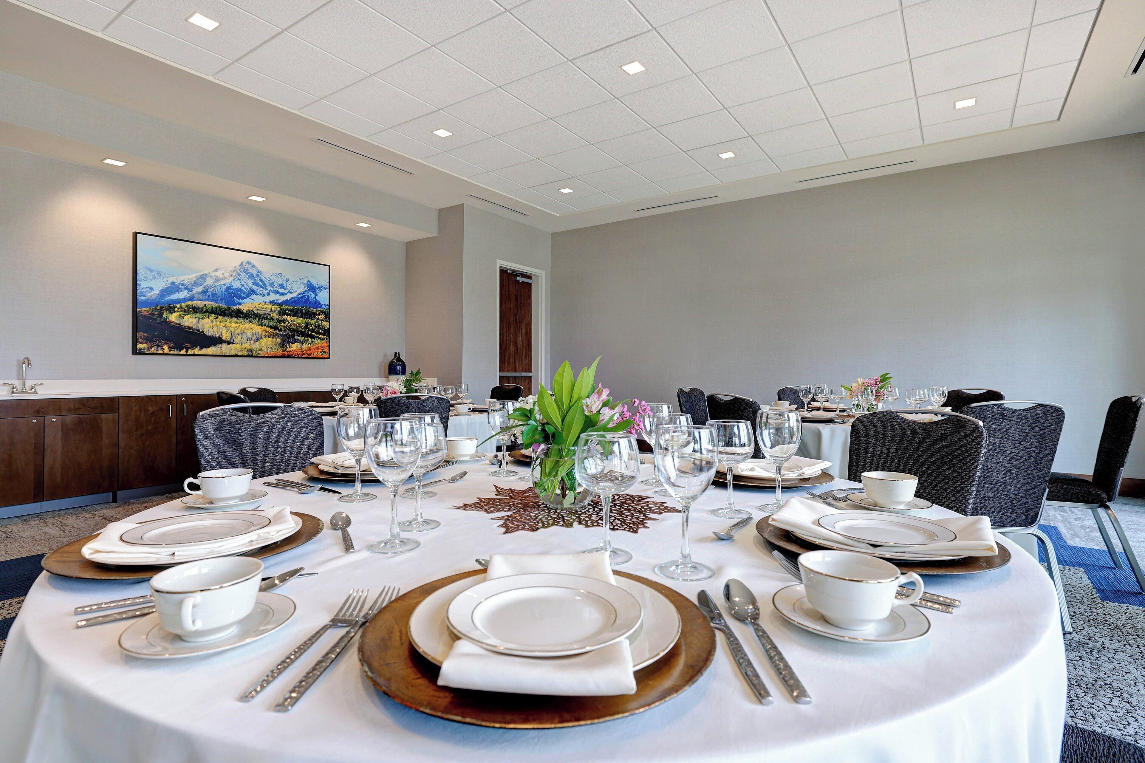 A conference room with round tables set for a meeting, equipped with white tablecloths, plates, cutlery, and glassware.
