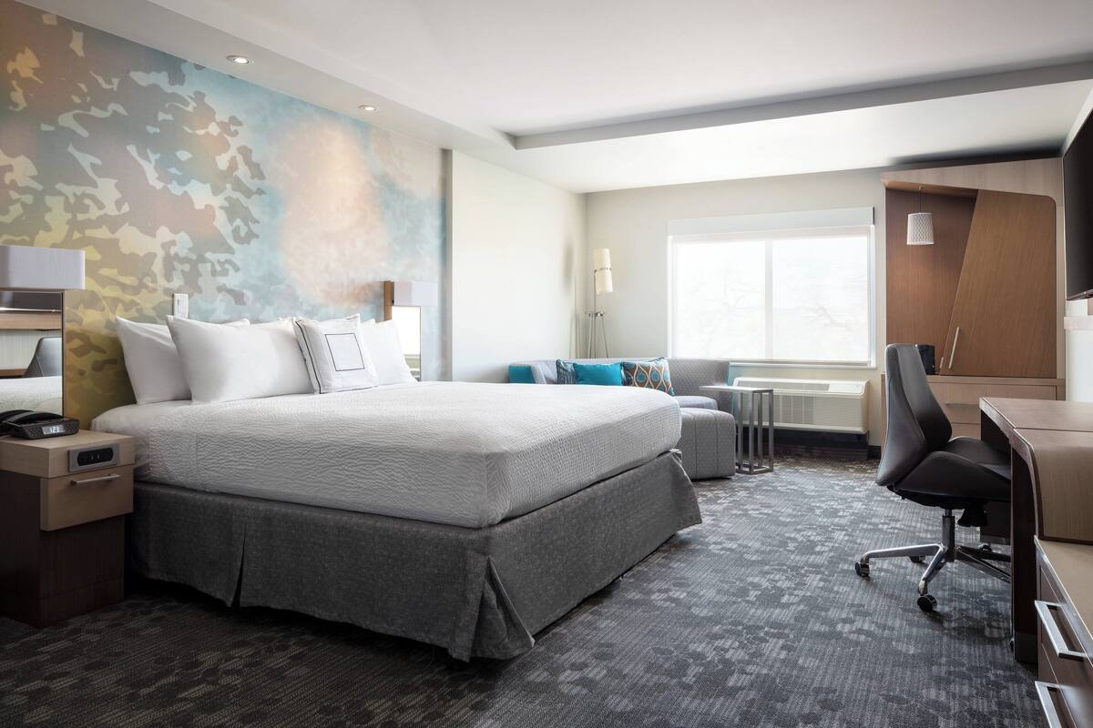 A modern hotel room with a large bed, a desk, a chair, and a couch.