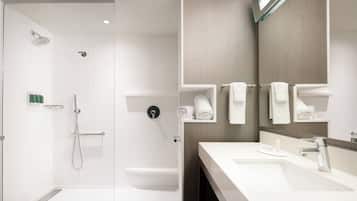 A modern bathroom with a glass-enclosed shower, a white sink, and a mirror with built-in towel racks.