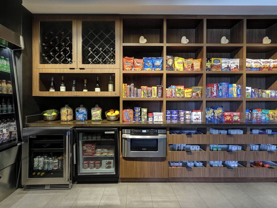 A self-service beverage and snack station with refrigerated drinks, a microwave, and shelves stocked with various snacks and packaged goods.
