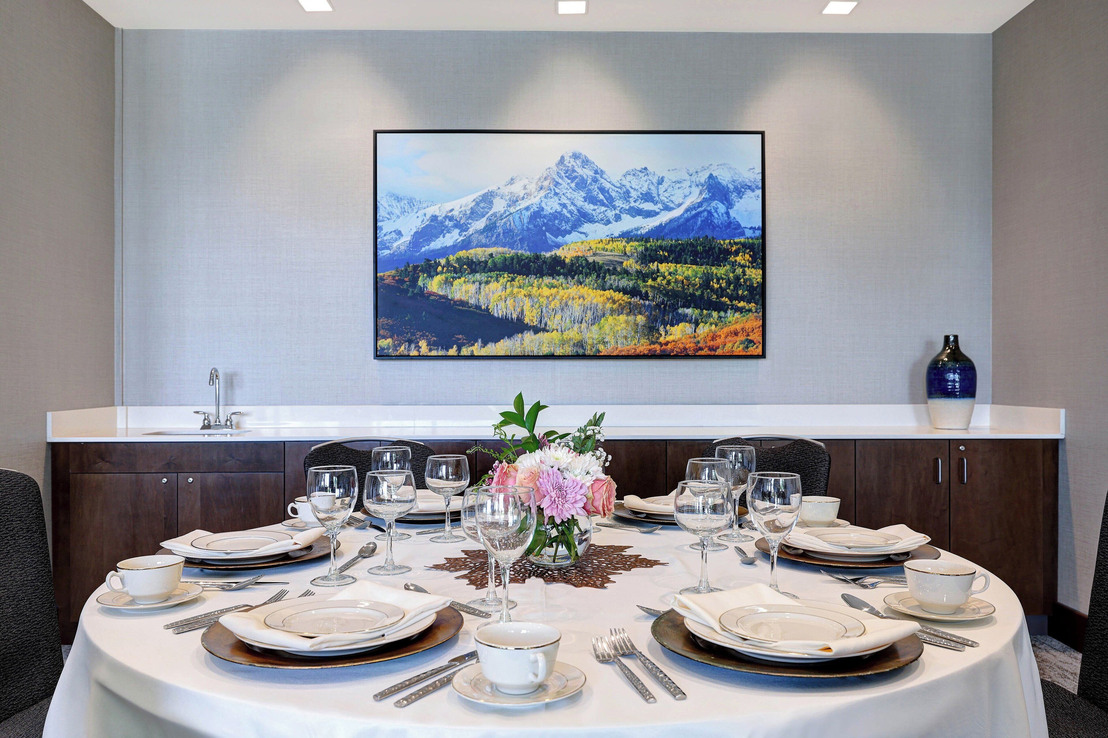 Mesa de jantar posta para seis pessoas, com uma pintura de paisagem montanhosa acima.