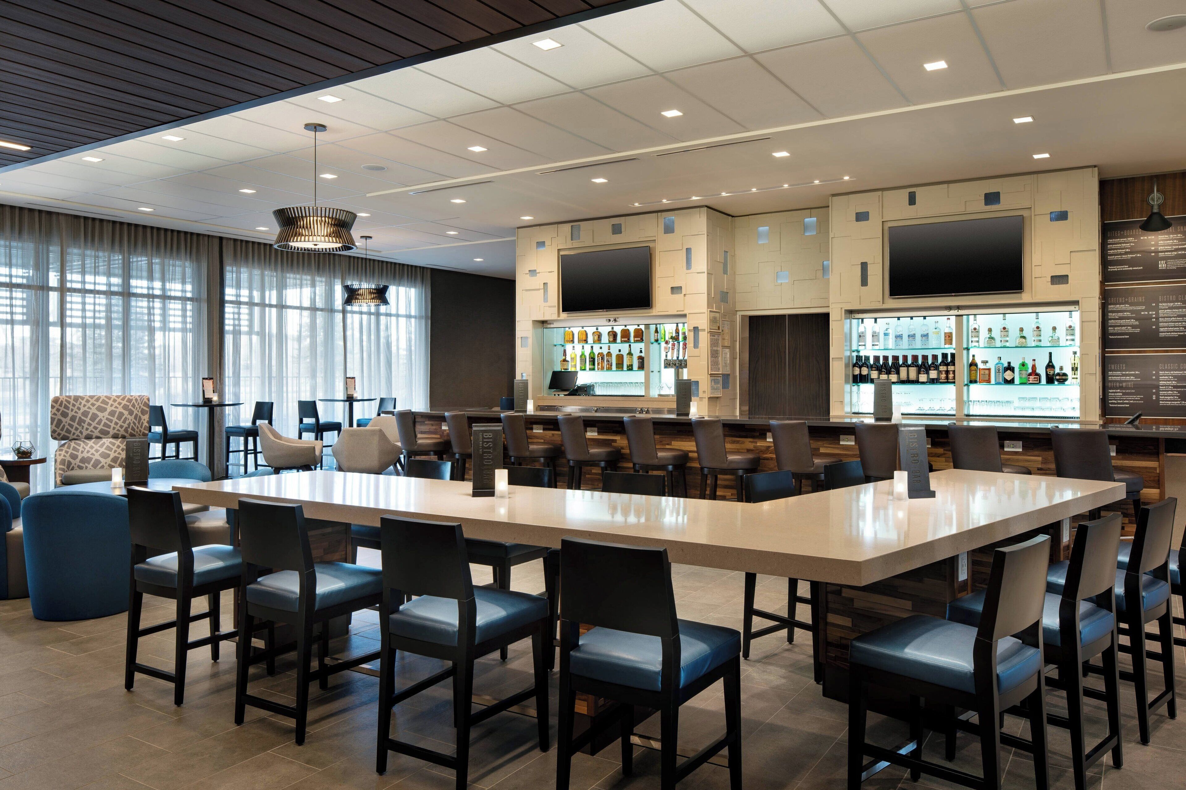 A modern bar area with a long counter, multiple seating options, and a television screen.