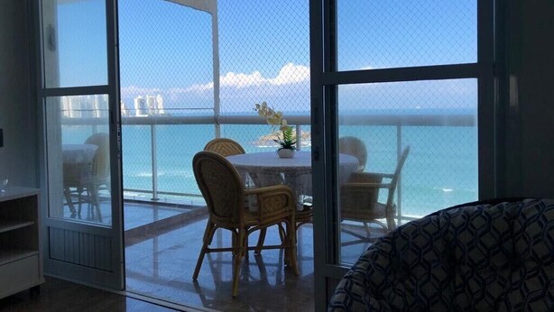 Un balcón con vista al mar, sillas de mimbre y una mesa con una planta en maceta.