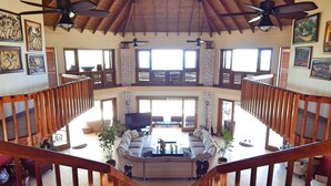 Amplio espacio habitable en varios niveles, con escalera de madera, ventiladores de techo y un gran conjunto de sofás.
