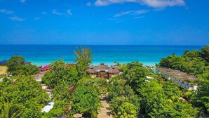 Un resort con edificios de techo de paja, una vista despejada del océano y exuberante vegetación.