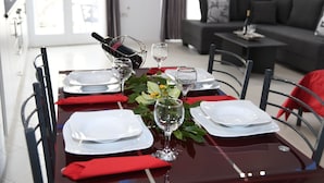 Een eettafel gedekt met witte borden, rode servetten en glazen wijnglazen, met een fles wijn in een draadmand.