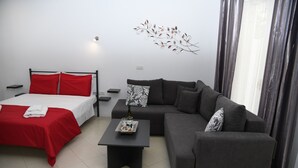 Een moderne slaapkamer met een bed, een grijze bank en een kleine tafel met een fles en glaasjes.