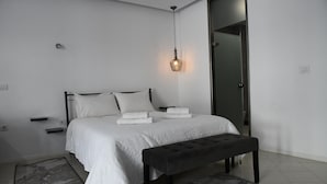 Een slaapkamer met een bed, twee nachtkastjes, een bankje en een hanglamp.