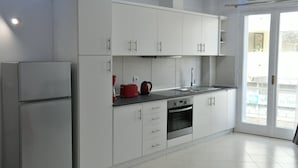 Een moderne keuken met witte kasten, een ingebouwde oven en een rode waterkoker op het aanrecht.