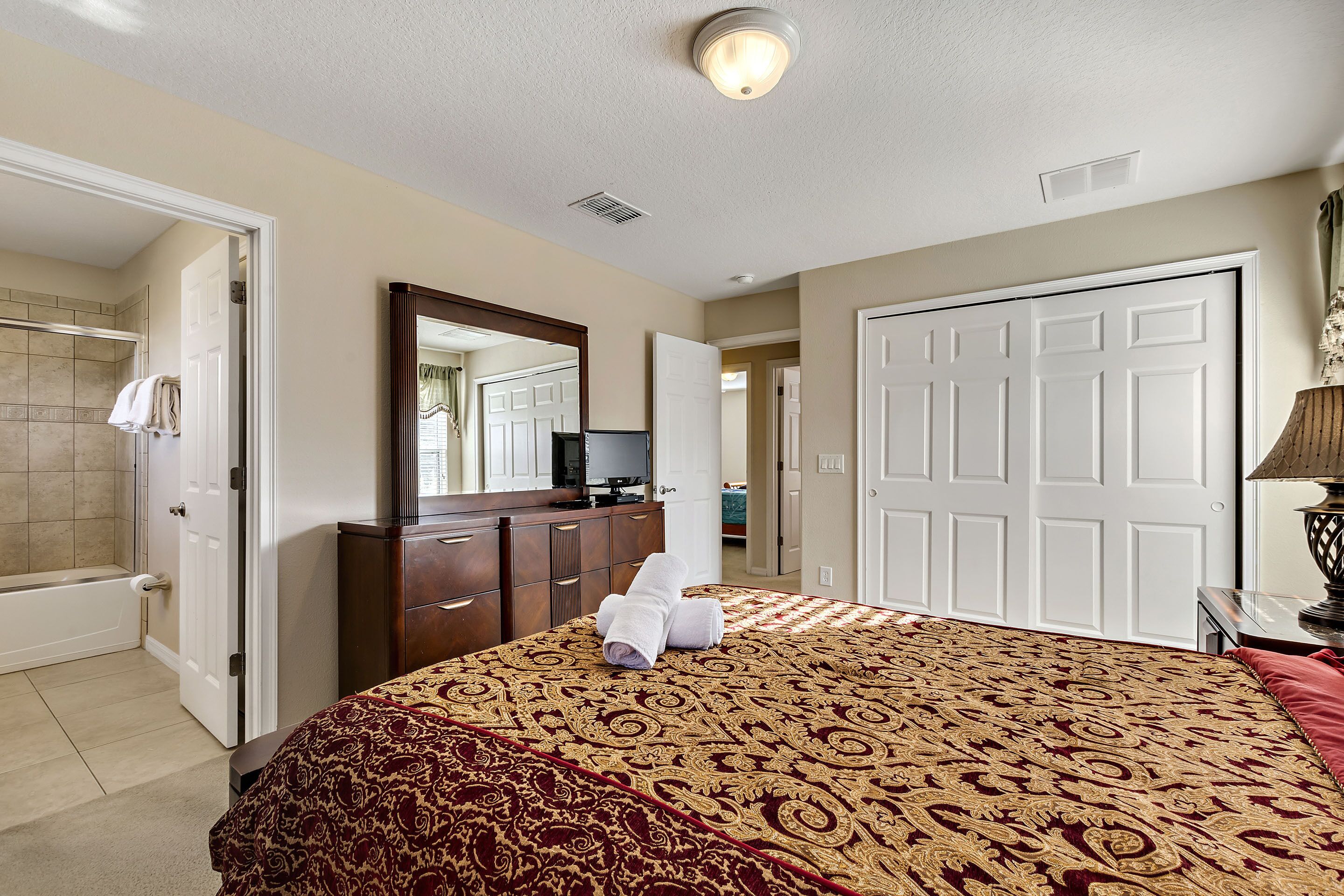 A bedroom with a large bed, a dresser, a television, and a bathroom with a shower and toilet.